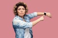 Your time is running out. Portrait of serious bossy young woman with curly hairstyle in casual blue shirt standing and pointing at