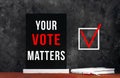 Your Vote Matters text sign on black chalkboard with white notebok and red pen on dark background. Make political choice