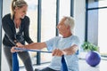 Youre doing a good job. a female physiotherapist helping a senior man stretch with a stretching band in a fitness centre