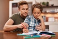 Youre doing well, buddy. a man sitting with his son while he does his homework.