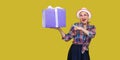 It is yours? Happy beautiful modern grandma in white hat and in checkered shirt standing, surprised holding big gift box with Royalty Free Stock Photo