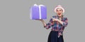 It is yours? Happy beautiful modern grandma in white hat and in checkered shirt standing, surprised holding big gift box with Royalty Free Stock Photo