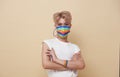 Youth asian transgender LGBT wear rainbow mask isolated over nude color background. gender expression pride and equality concept