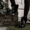 Youth fashionable black warm boots close-up. Young trendy woman in winter stylish shoes with fur stands near old chest in the room