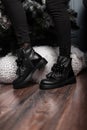 Youth fashionable leather black women`s winter boots. Stylish young woman in jeans in trendy shoes stands in a room near beautifu