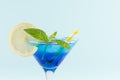 Youth fresh alcohol blue Hawaii cocktail with licor curacao, ice cube, lemon slice, yellow straw in wine glass on mint background.