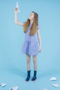 Youth Lifestyle. Teenager Girl in Blue Checked Dress and Rubber Boots Launching Origami Paper Plane Over Blue Background