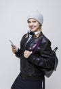 Youth Lifestyles. Portrait of Smiling Happy Caucasian Blond Girl in Warm Hat and Leather Jacket Posing With Cellphone and Backpack