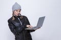 Youth Lifestyles.Suspicious Caucasian Blond Femalr in Warm Hat and Leather Jacket Posing With Laptop on White Background