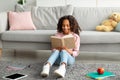 Youth and literature. Smiling african american gen z girl holding and reading paper book, sitting on the floor carpet Royalty Free Stock Photo