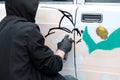 Youth subculture. A guy in black clothes and gloves draws on a white car an abstract image in the style of graffiti. Vandalism or