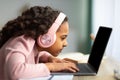 Youth and technology concept. Focused black schoolgirl using laptop computer, sitting at table too close to pc, side Royalty Free Stock Photo