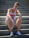 A youth in a white T-shirt and shorts with a lemonade on stone stairs background. Recreation, dynamic and fashion