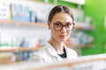 A youthful pleasant dark-haired girl with glasses, wearing a medical overall,stands next to the shelf in a modern