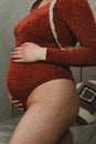 Youthful pregnant woman wearing a brown body suit tenderly cradles her baby bump