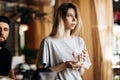 A youthful pretty blonde girl,dressed in casual style, holds a clean glass and looks at the window in a modern coffee