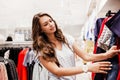 A youthful pretty lady with long hair,wearing casual clothes, is choosing a new dress in a famous shop.