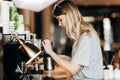 A youthful pretty thin blonde with long hair,dressed in casual outfit,is cooking coffee in a modern coffee shop. Process