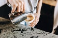 A youthful slim kind blonde girl,dressed in casual outfit,skillfully adds milk to coffee in a modern coffee shop.