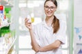 A youthful thin brown-haired lady with glasses,dressed in a lab coat,is holding a small jar in her right hand in a new