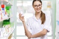 A youthful thin brown-haired lady with glasses,dressed in a lab coat,is holding a small jar in her right hand in a new