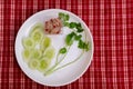 Yum small tuna salad in a clear plastic cup and place it on a white plate with coriander and sliced cucumber. Red plaid background