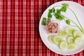 Yum small tuna salad in a clear plastic cup and place it on a white plate with coriander and sliced cucumber.