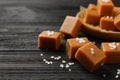 Yummy caramel candies and sea salt on black wooden table, , closeup. Space for text