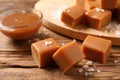 Yummy caramel candies and sea salt on wooden table, closeup