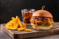 Yummy chicken burger with cheese, fries and a glass of cola on a wooden board on a dark background Royalty Free Stock Photo