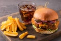 Yummy chicken burger with cheese, fries and a glass of cola on a wooden board on a dark background Royalty Free Stock Photo