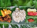 A Yummy Delight: A Nasi Liwet on a Banana Leaf with a Fried Chicken, Tomato,Spicy Sambal, Cucumber, Green Peas, Tofu, and Tempeh
