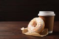 Yummy donut and paper cup on table against brown background, space for text Royalty Free Stock Photo