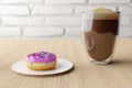 Yummy donut with pink icing and colorful sprinkles and cup of coffee with foam on wooden table background. Royalty Free Stock Photo