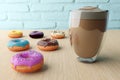 Yummy donuts with colorful icing and colorful sprinkles and cup of coffee with foam on wooden table background.