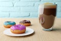 Yummy donuts with colorful icing and colorful sprinkles and cup of coffee with foam on wooden table background.
