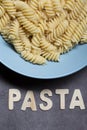 Yummy white fusilli Italian pasta food served on a white plate with pasta wooden letters written