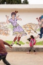 A group of chinese elementary schoolchildren walking pass the hand drawn traditional art of tribe Yunnanese on the village wall.