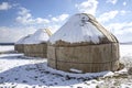 Yurts under the snow in the middle of a snow-covered field against a sky with clouds. travel Kyrgyzstan