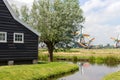 Old dutch windmills, pond and wooden house in historical village. Holland mills in field with river and ancient building.