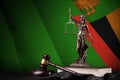 Zambia flag with statue of lady justice, constitution and judge hammer on black drapery. Concept of judgement and guilt Royalty Free Stock Photo