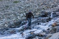 An Indian trekker crossing a stream on a rocky hillside while hiking in the Himalayan region of