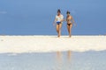 Two girls in swimsuits go to the ocean on the tropical sand beach of Zanzibar island, Tanzania, East Africa