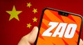 ZAO app logo on the screen of smartphone and the blurred flag of China on the screen behind. Zao is currently a number one enterta