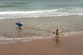 Surfers going in and out on the beach on a cloudy day.