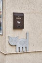 Mailbox and flat sculpture of smiling cat walking on pipe on wall with fish in its stomach.