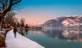 Zell am See in winter evening. Esplanade along Lake Zell, town, mountains and snow with reflections in water. Famous ski