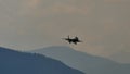 Small silhouette of a military jet plane landing with blue mountains in background