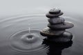 Zen stones in balanced pile in water on rippled water surface and water drop.