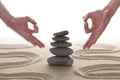 Zen stones piled on raked sand with two hands in om position and copy space for your text